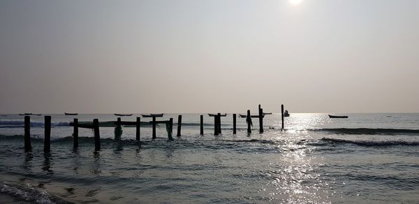 Wooden posts in sea against clear sky