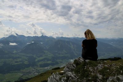 Rear view of woman sitting on mountain against sky