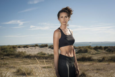 Fit woman standing wearing sports bra and leggings at the beach