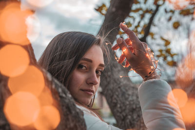 Portrait of young woman holding illuminated string light
