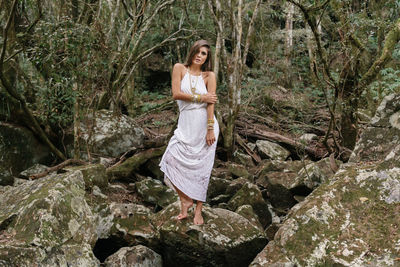 Portrait of young woman standing on rock in forest