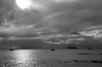 Sailboats and sailing ship in sea against cloudy sky