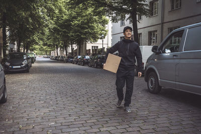 Smiling delivery man with package while walking on street in city