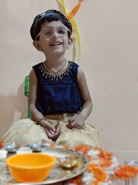 Smiling girl wearing eyeglasses sitting against wall at home