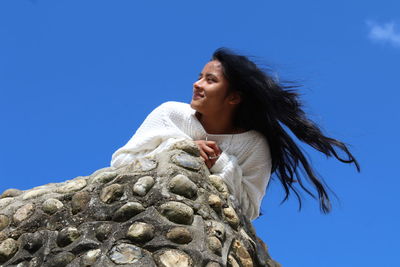 Low angle view of young woman lying on mountain against blue sky during sunny day