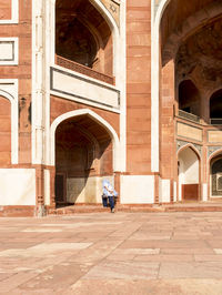 Rear view of woman walking towards historical building during sunny day