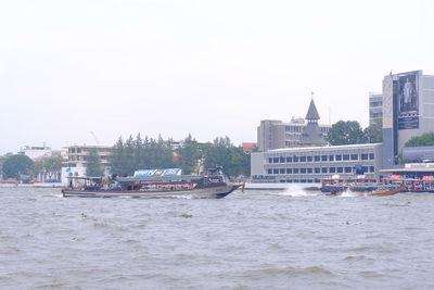 Boats in river by city against clear sky