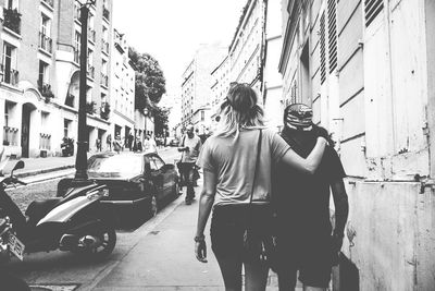 Rear view of people walking on street amidst buildings in city