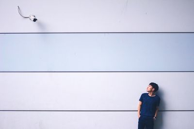 Young asian man standing against wall looking at surveillance camera