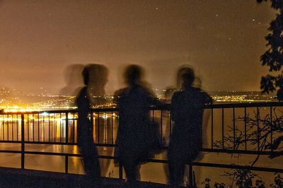 Silhouette people standing by railing against sky at night