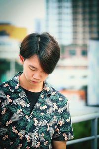 Young man looking down while standing against buildings