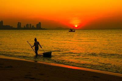 Silhouette man standing in sea against orange sky