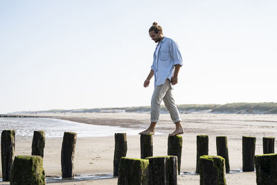 Man standing on wooden post by sea against sky