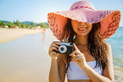 Young woman holding hat against sky