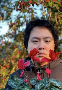 Portrait of young asian man holding red flowering cyclamen plant.