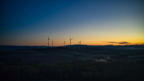 Wind turbines on landscape against sky during sunset