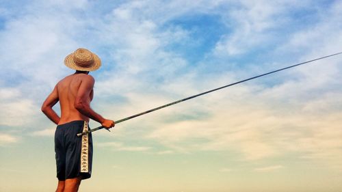 Low angle view of man fishing against sky