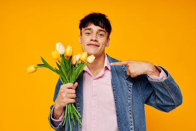 Portrait of young man showing tulip against yellow background