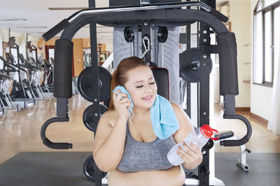 Fat woman looking at water bottle while sitting in gym