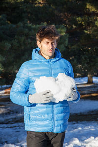 Young man holding heart shape snow during winter