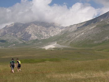 People walking on mountain road against cloudy sky