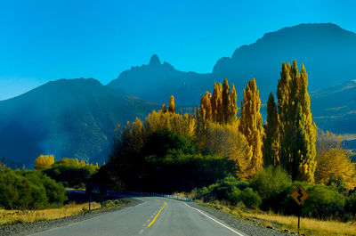 Empty road along trees and mountains against sky