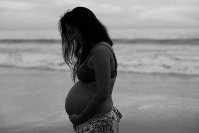 Side view of woman standing at beach against sky