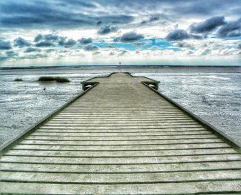 Pier on sea against cloudy sky