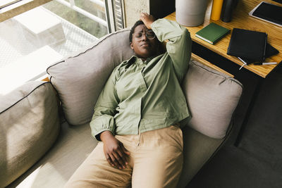 High angle view of businesswoman with headache lying on sofa against window at office