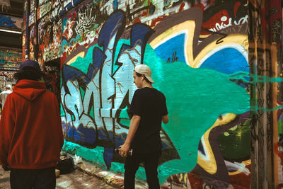 Rear view of man standing against graffiti wall