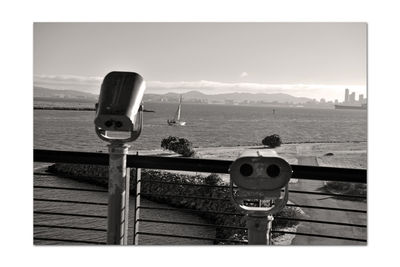 Rear view of coin-operated binoculars by sea against sky