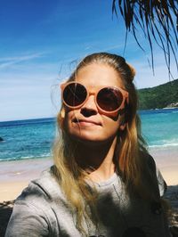 Portrait of woman wearing sunglasses at beach against sky