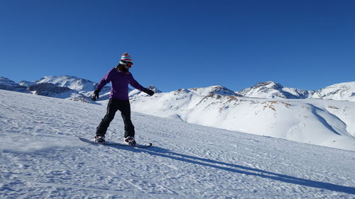 Full length of woman snowboarding against clear blue sky