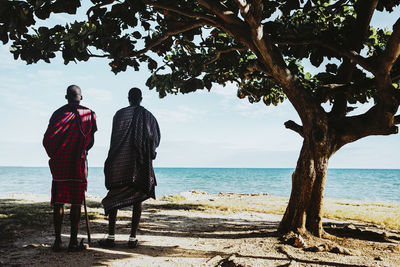 Two masai men in traditional clothes standing under big mkungu tree