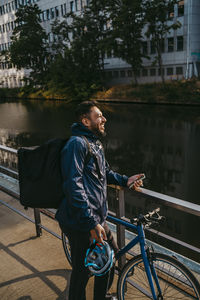 Smiling male food delivery person standing near railing with bicycle