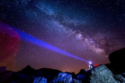 Low angle of tourist with headlamp sitting on cliff and admiring amazing starry sky at night in pyrenees