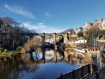 Bridge over river by buildings against sky