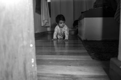 Full length of cute girl crawling on wooden floor at home