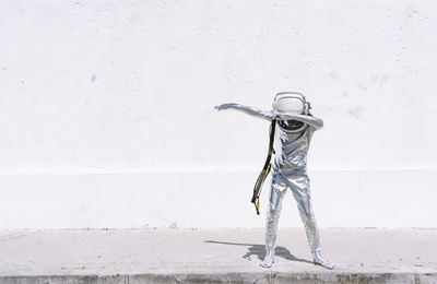 Boy in astronaut costume dabbing movement while standing against wall