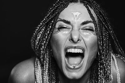 Close-up of young woman screaming against black background