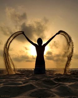 Silhouette person throwing sand against cloudy sky