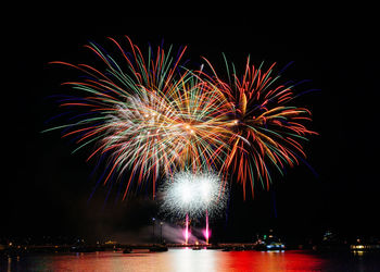 Firework display reflecting on river against sky at night