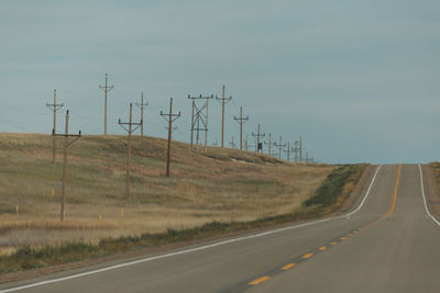 Road by electricity pylon against sky