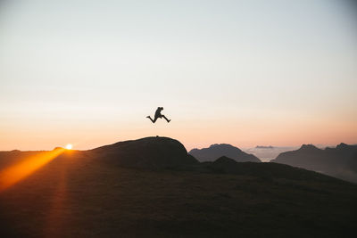 Silhouette of man jumping against mountains during sunset