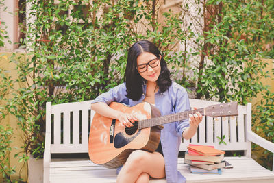 Woman playing guitar while sitting on bench at park