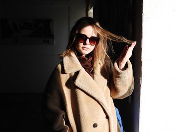 Portrait of young woman wearing sunglasses standing against wall