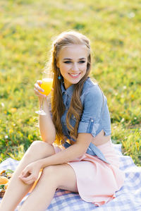 Attractive cheerful girl sitting on a blanket and spending the weekend relaxing in the park outdoors