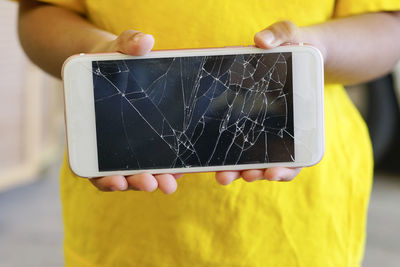 Midsection of boy holding damaged mobile phone