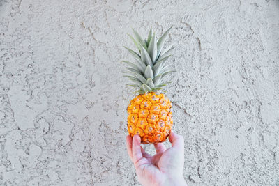 Cropped hand of man holding pineapple against wall