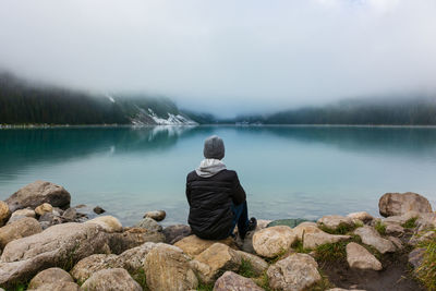 Rear view of man sitting on rock against lake